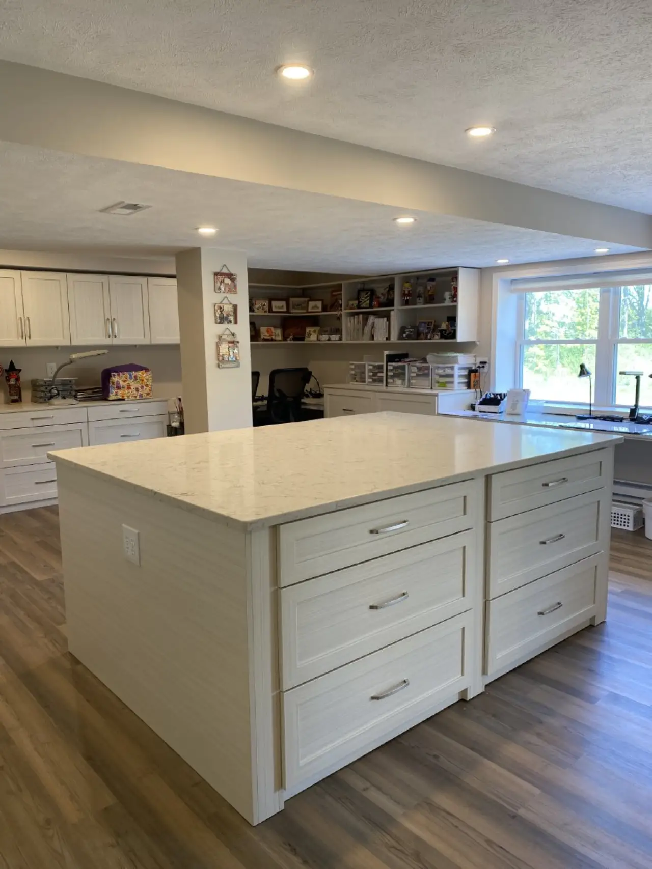 A spacious craft room with a large island, white cabinets, and wooden floors.