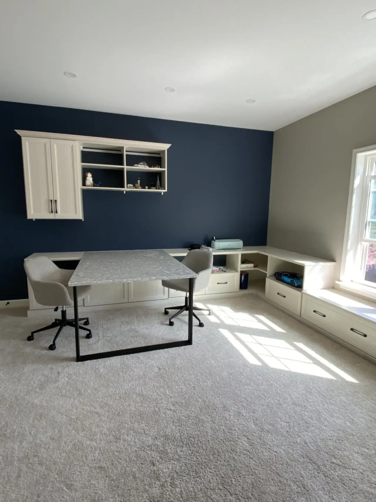 Home office with two chairs, built-in shelves, a deep blue accent wall, and a window seat.
