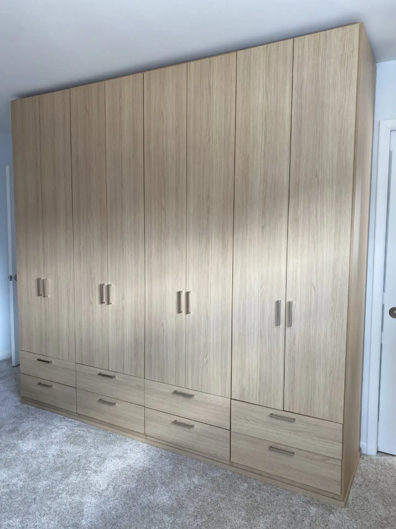 Large wooden wardrobe with six doors and six drawers, standing on a light carpeted floor.