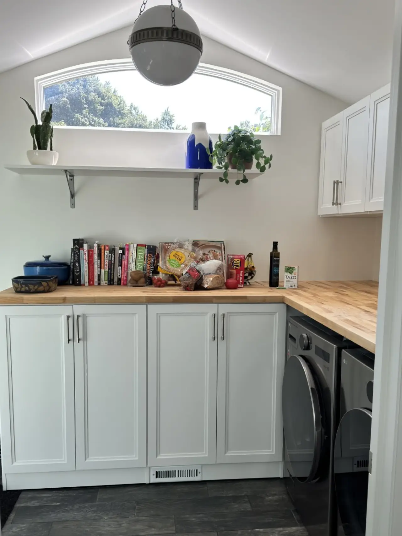 Small kitchen with white cabinets, books, plants, and groceries on a wooden countertop.