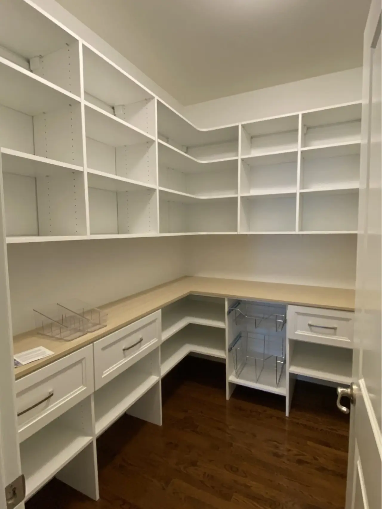 A walk-in pantry with white shelves, drawers, wooden countertop, and dark hardwood floors.
