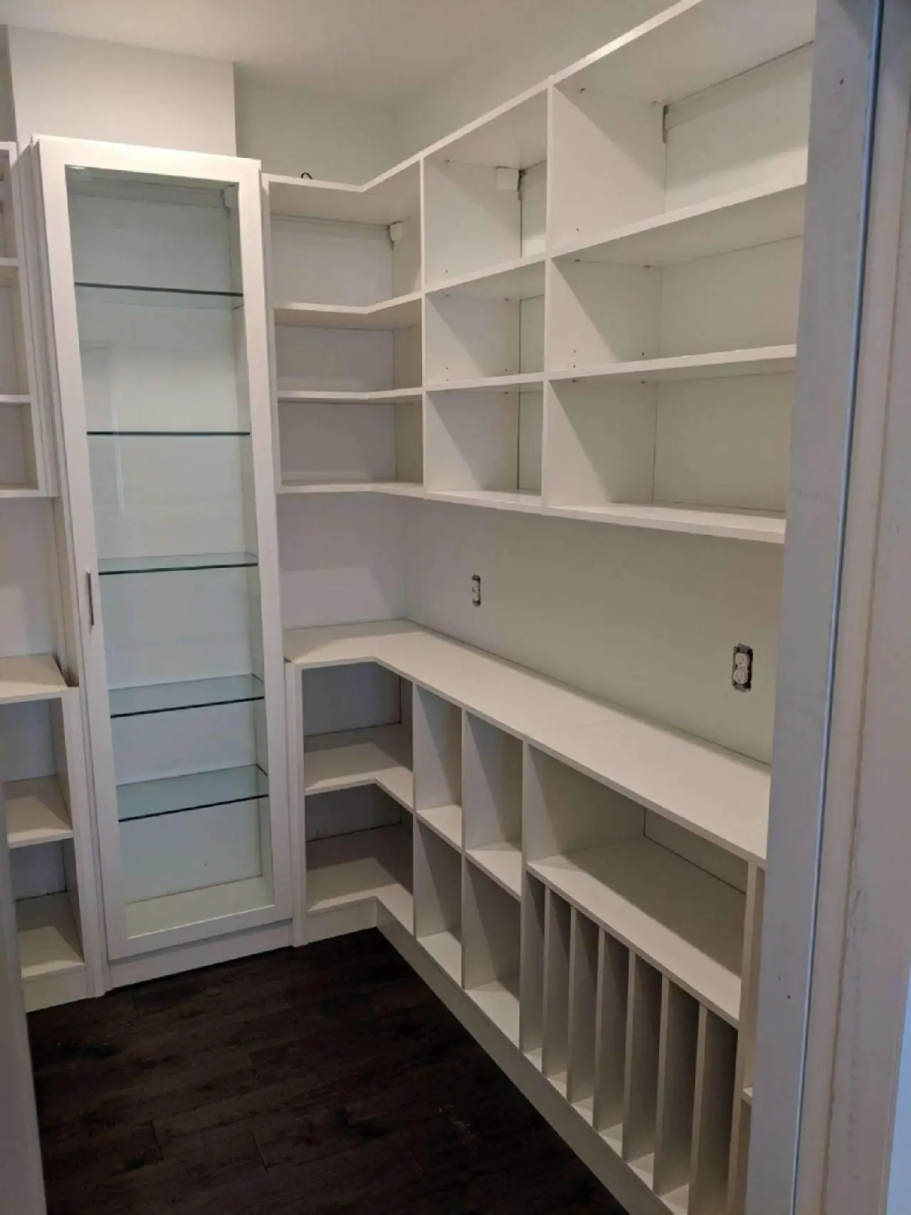 White built-in shelves and cabinets in an empty pantry or storage room with dark wood flooring.