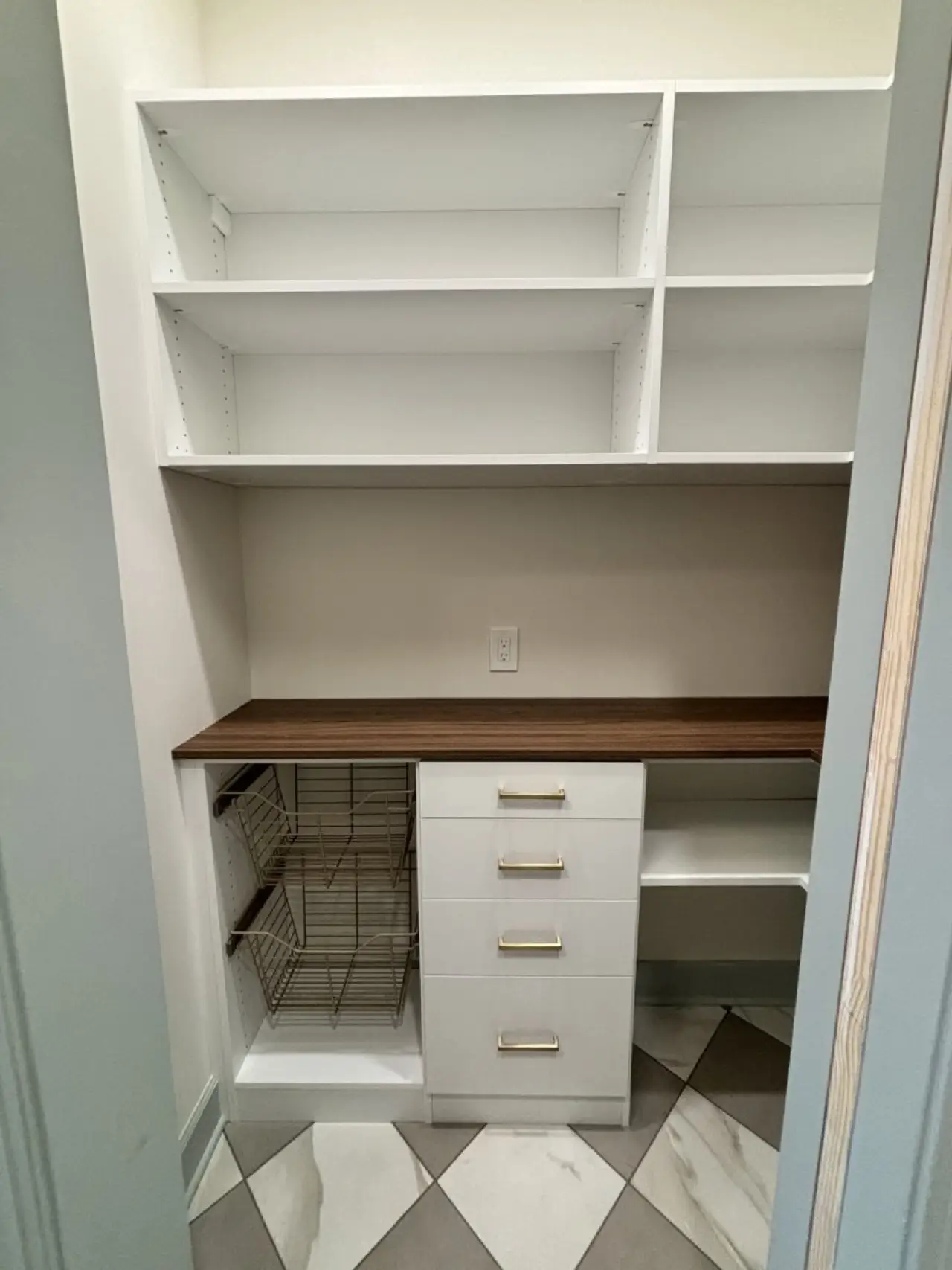 Small walk-in closet with white shelves, drawers, pull-out baskets, and a wooden countertop.