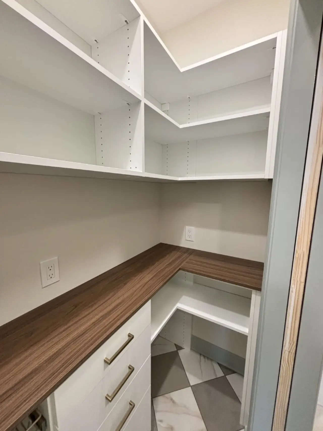 Walk-in pantry with white shelves, wood countertop, drawers, and patterned tile floor.