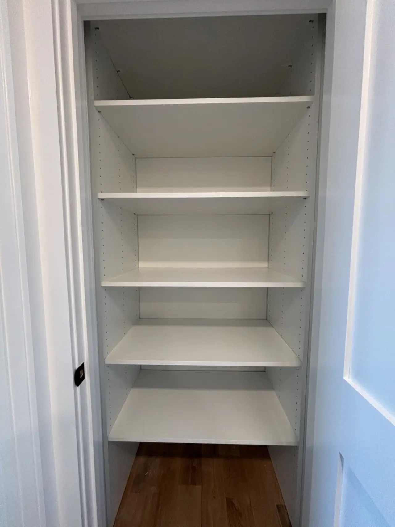 Empty white shelving unit with five shelves inside a small closet with wooden flooring.