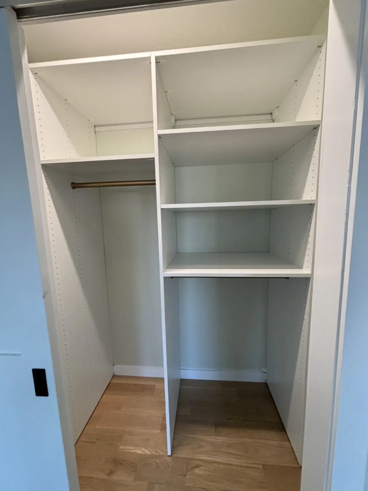 Empty white closet with shelves on the right and a hanging rod on the left, wood floor.