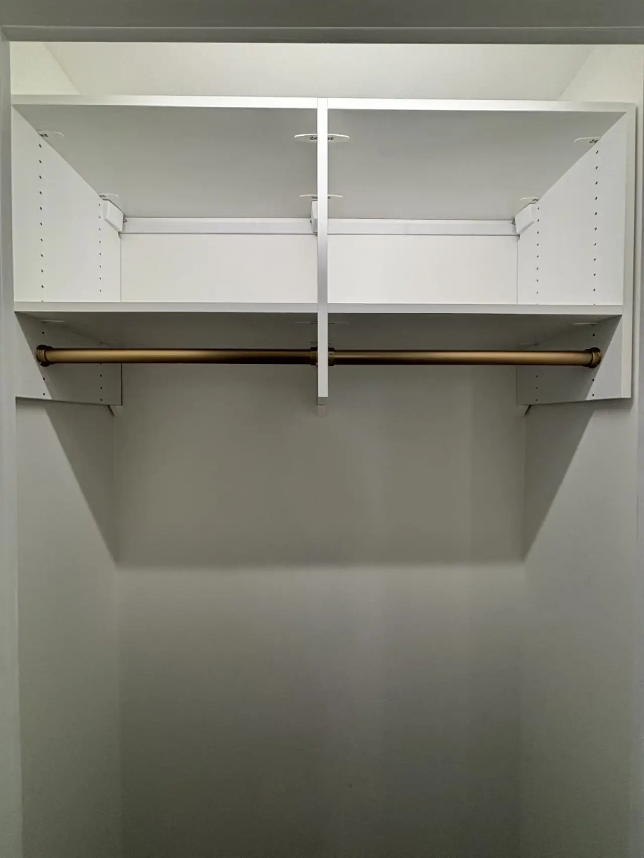 Empty white closet with a gold hanging rod and two open upper shelves.