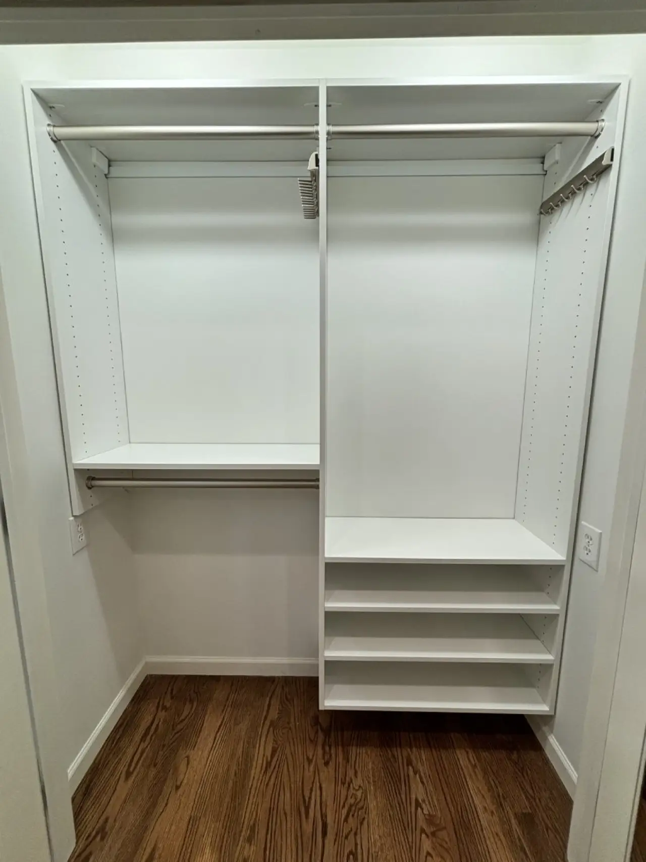 Empty white closet with shelves, hanging rods, and wooden floor.