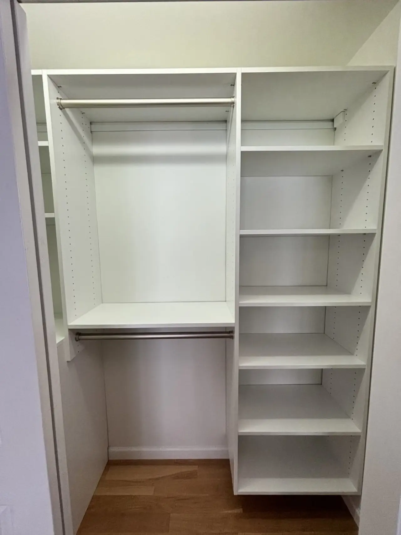 Empty white closet with shelves on the right and two hanging rods on the left, wooden floor.
