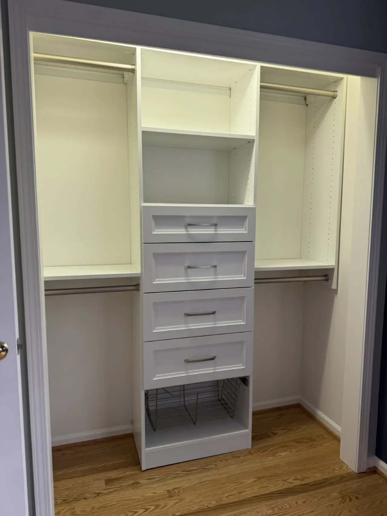 White walk-in closet with shelves, drawers, and hanging rods, on a hardwood floor.