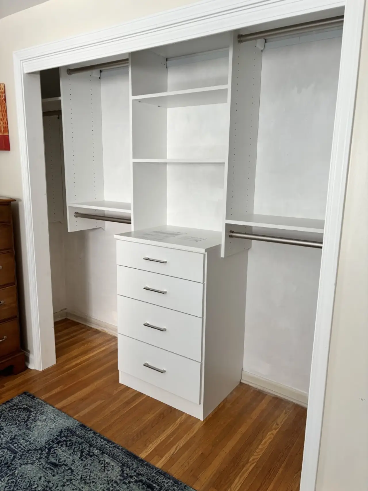 White closet organizer with shelves, drawers, and hanging rods in an empty closet space.