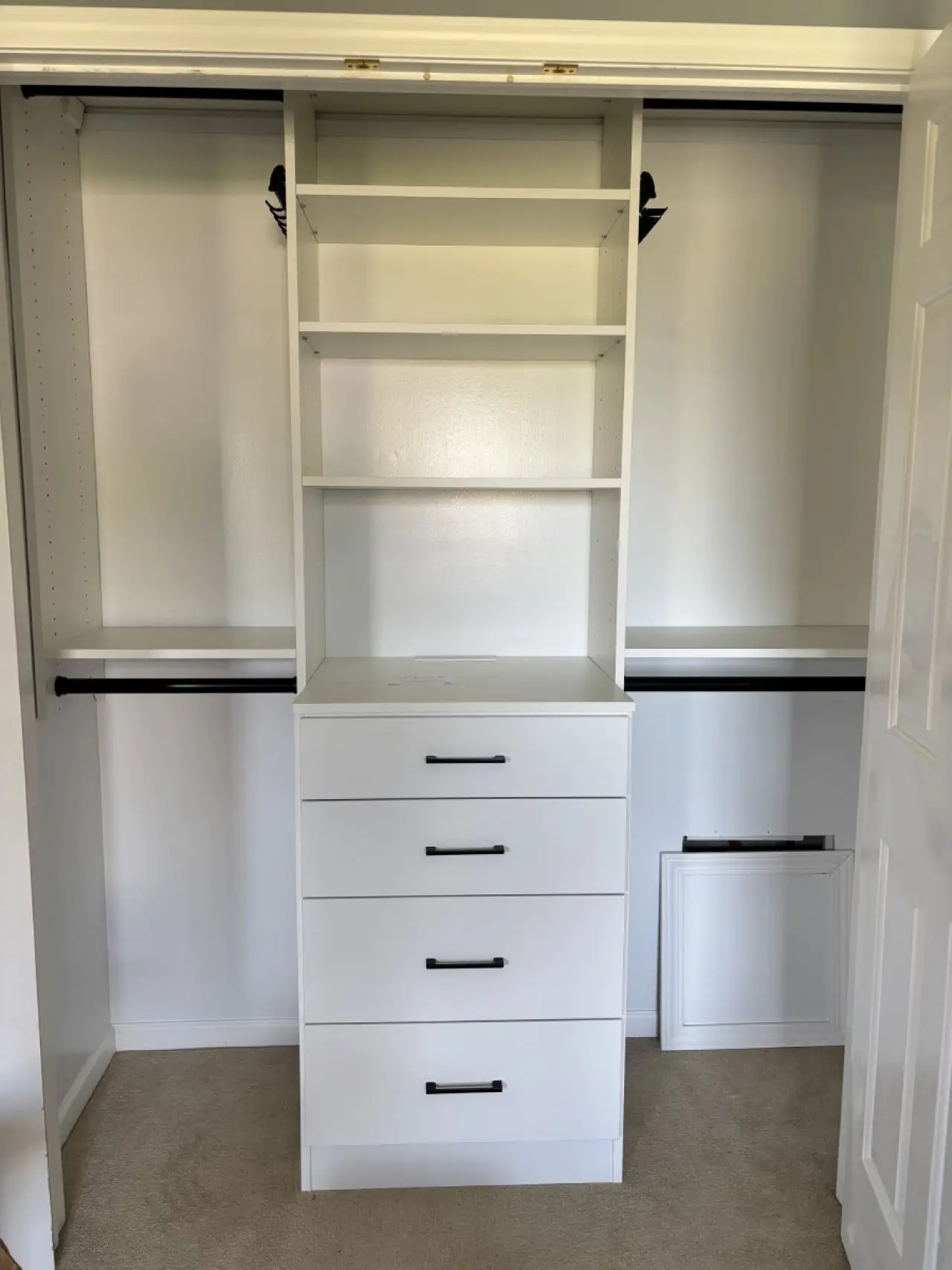 White closet organizer with shelves, four drawers, and two hanging rods on each side.