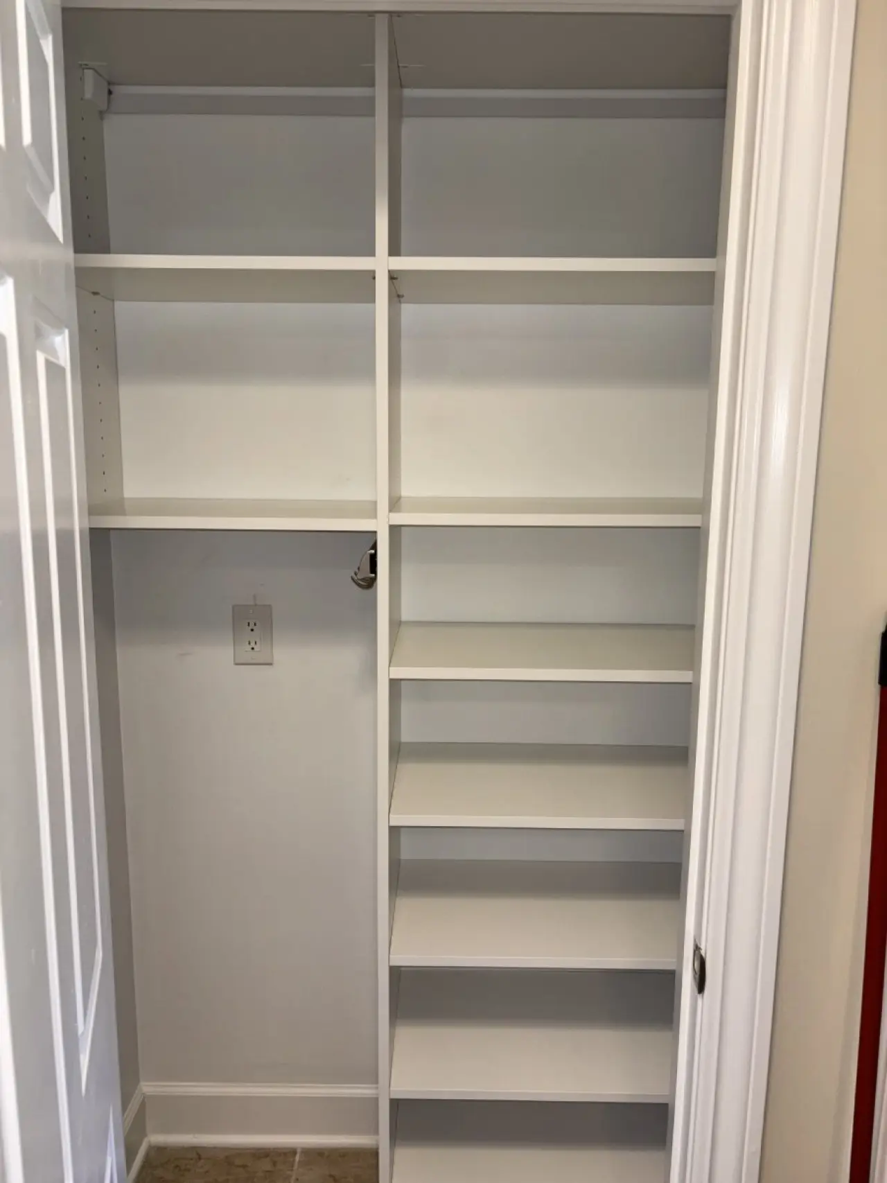 White closet with multiple empty shelves and a power outlet on the back wall.