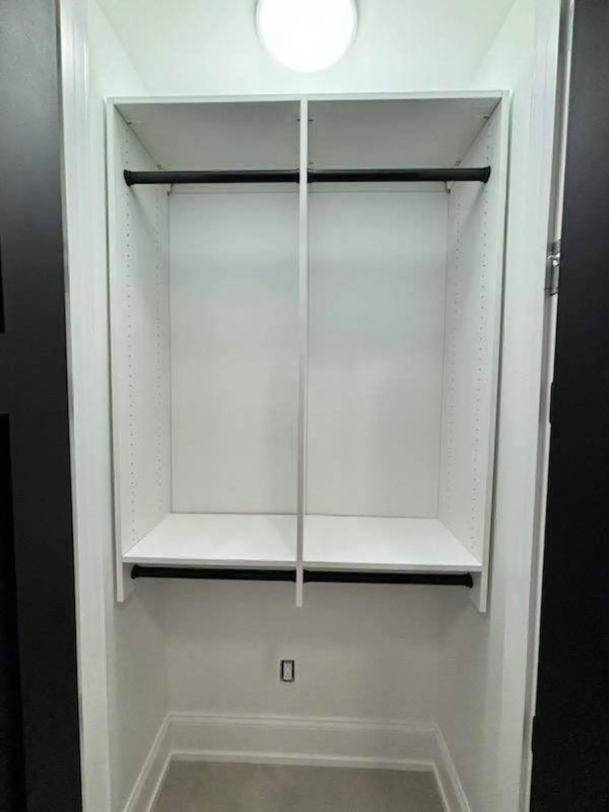 Empty white closet with two black hanging rods and shelves, viewed from the doorway.