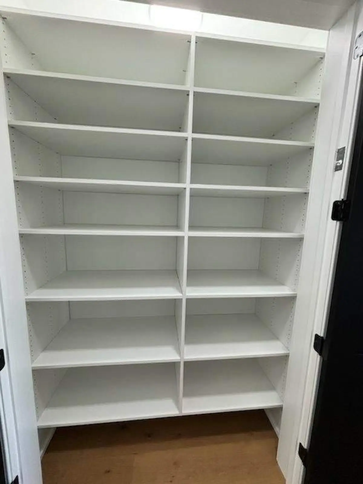 Empty white built-in shelving unit with five rows and four columns in a small room.