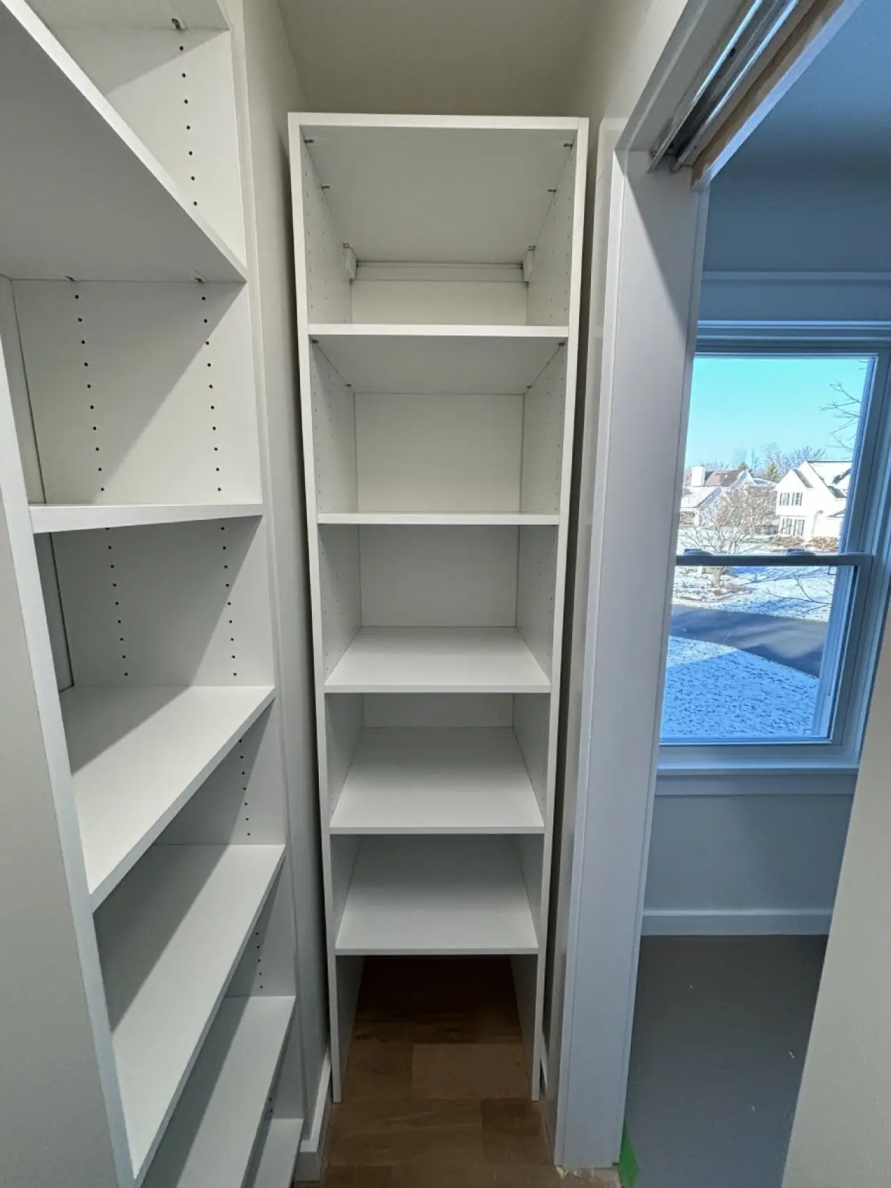 Tall, empty white shelves in a small room with a window showing a snowy neighborhood outside.
