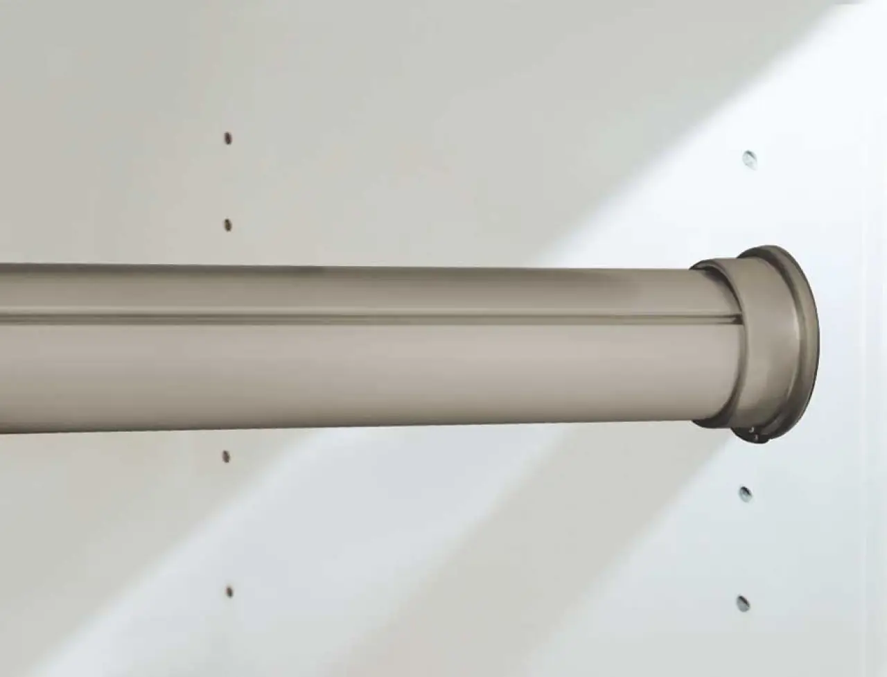 Close-up of a metallic closet rod mounted between white walls with shelving holes visible.