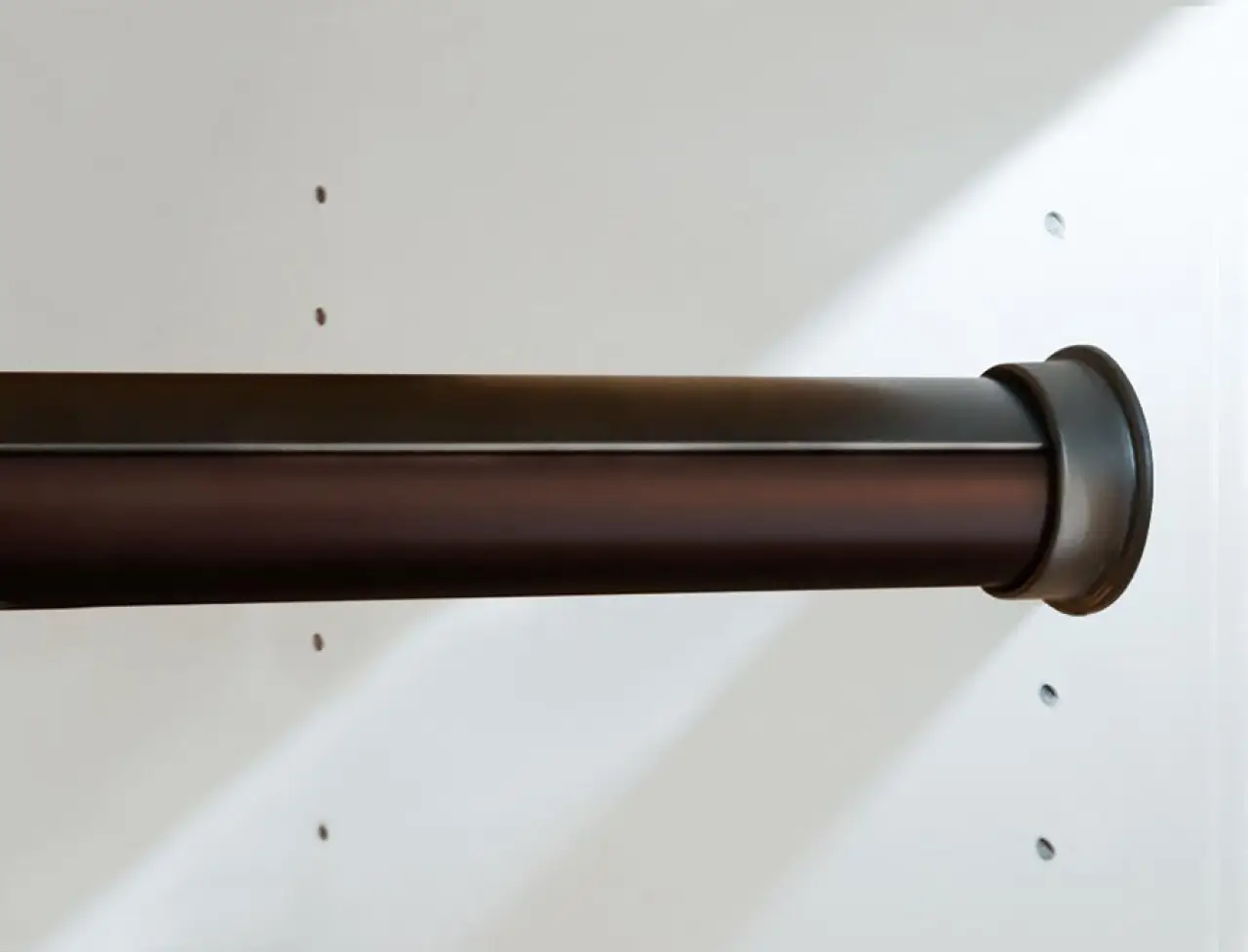 Close-up of a dark metal closet rod attached to a white wall with small holes nearby.