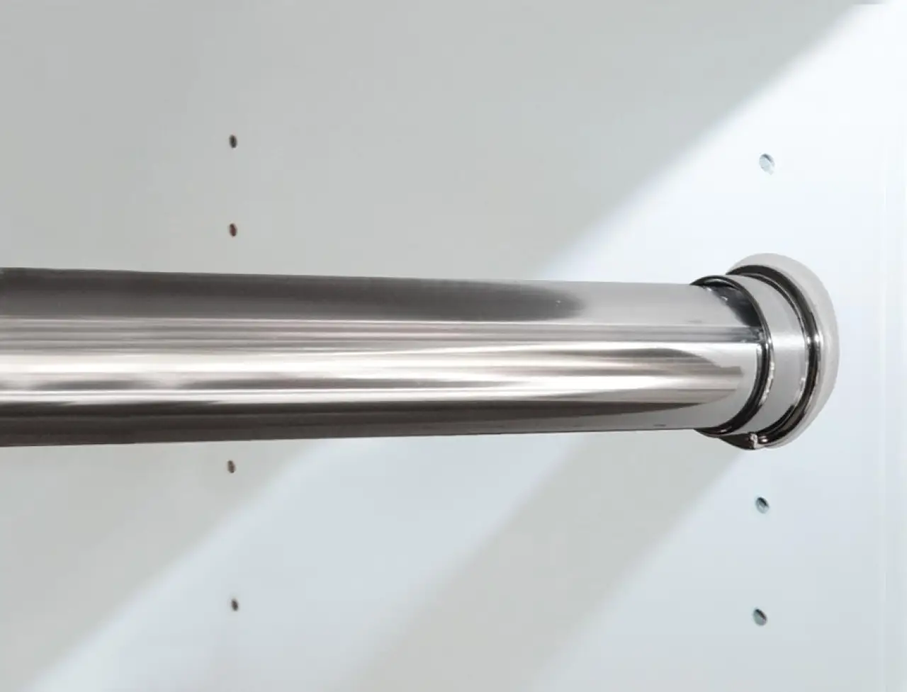 Close-up of a metal closet rod mounted on a white wall with small holes nearby.