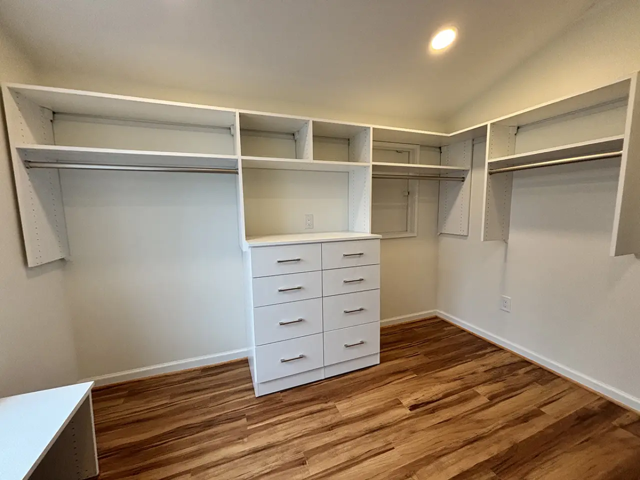 White walk-in closet with drawers, open shelves, hanging rods, and wood floor.