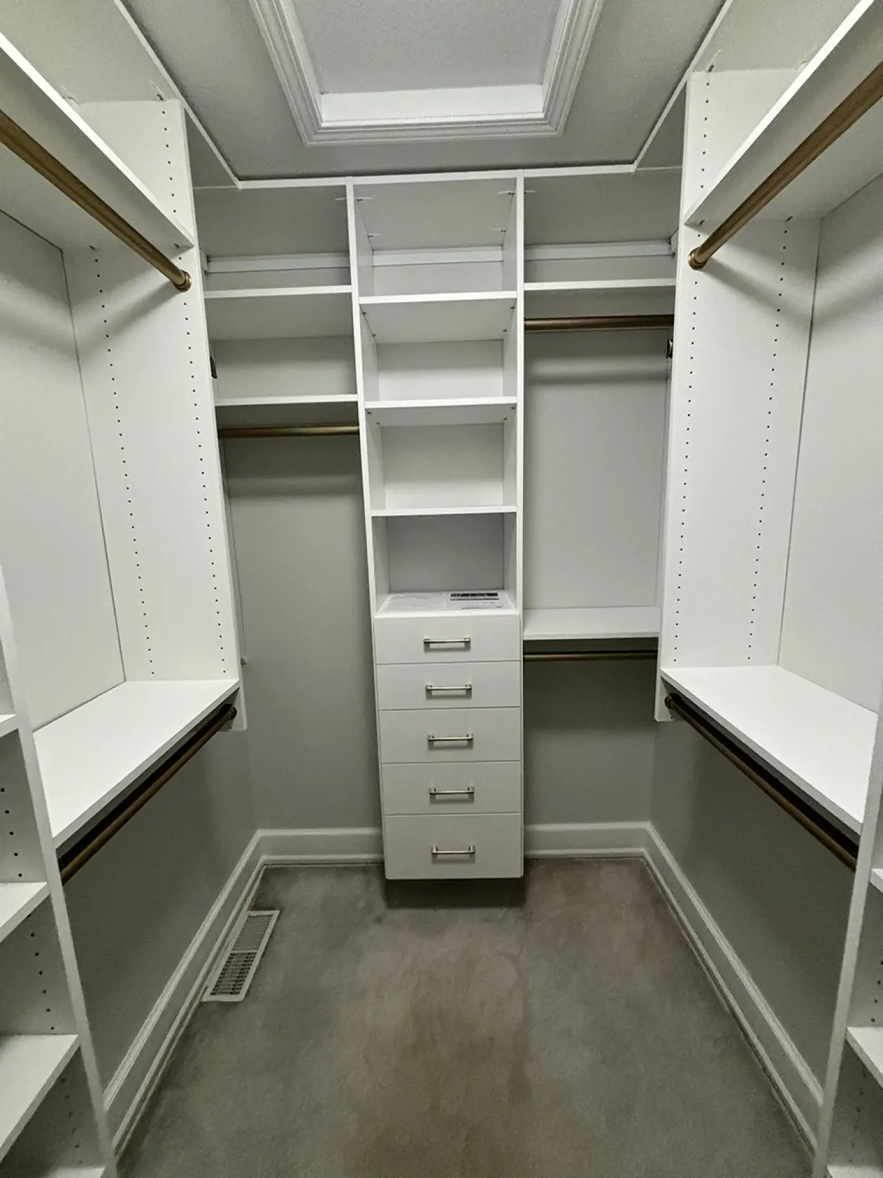 White walk-in closet with shelves, drawers, and hanging rods, and a vent on the floor.