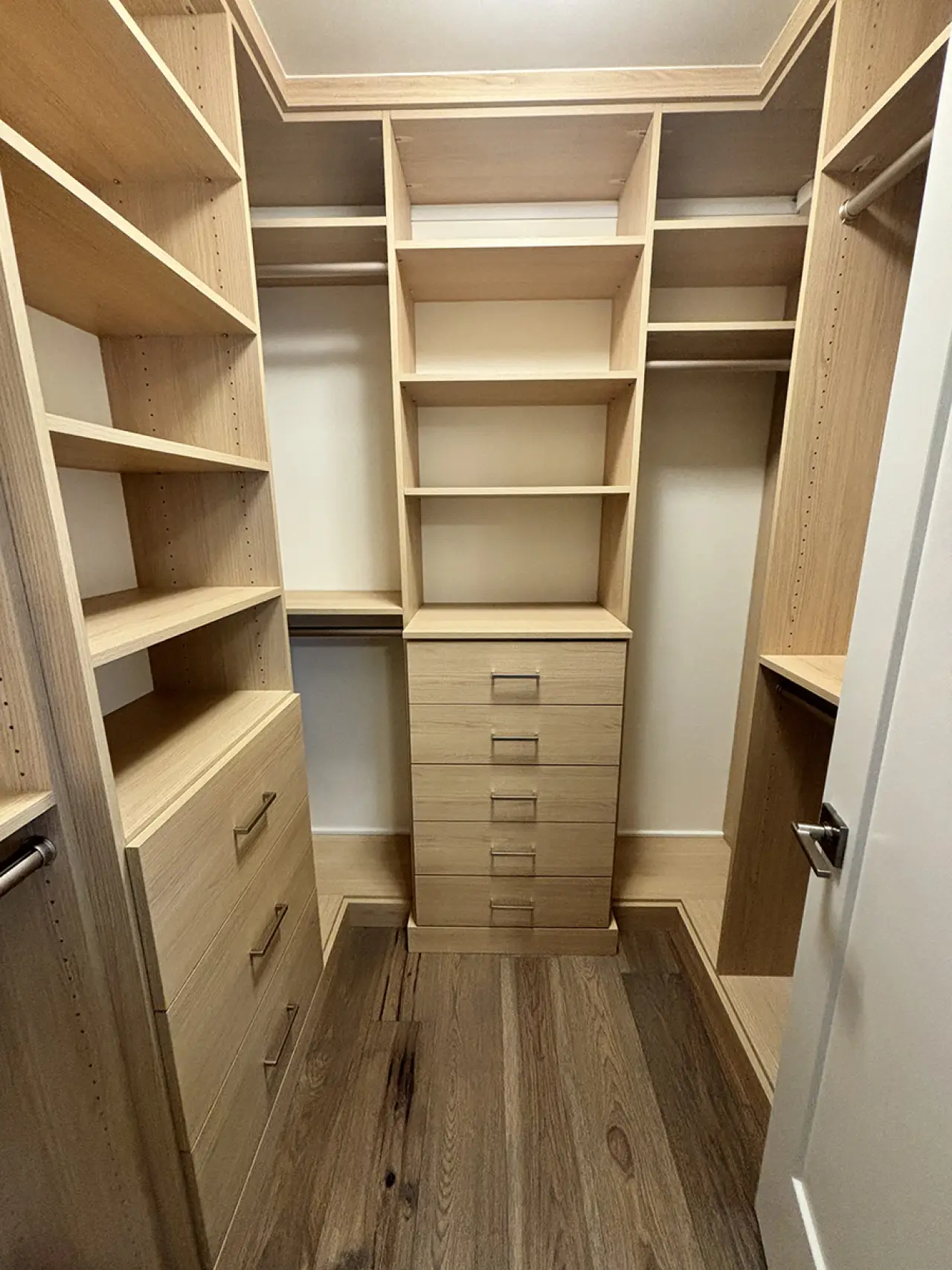Walk-in closet with wooden shelves, drawers, and hanging rods, empty and organized.