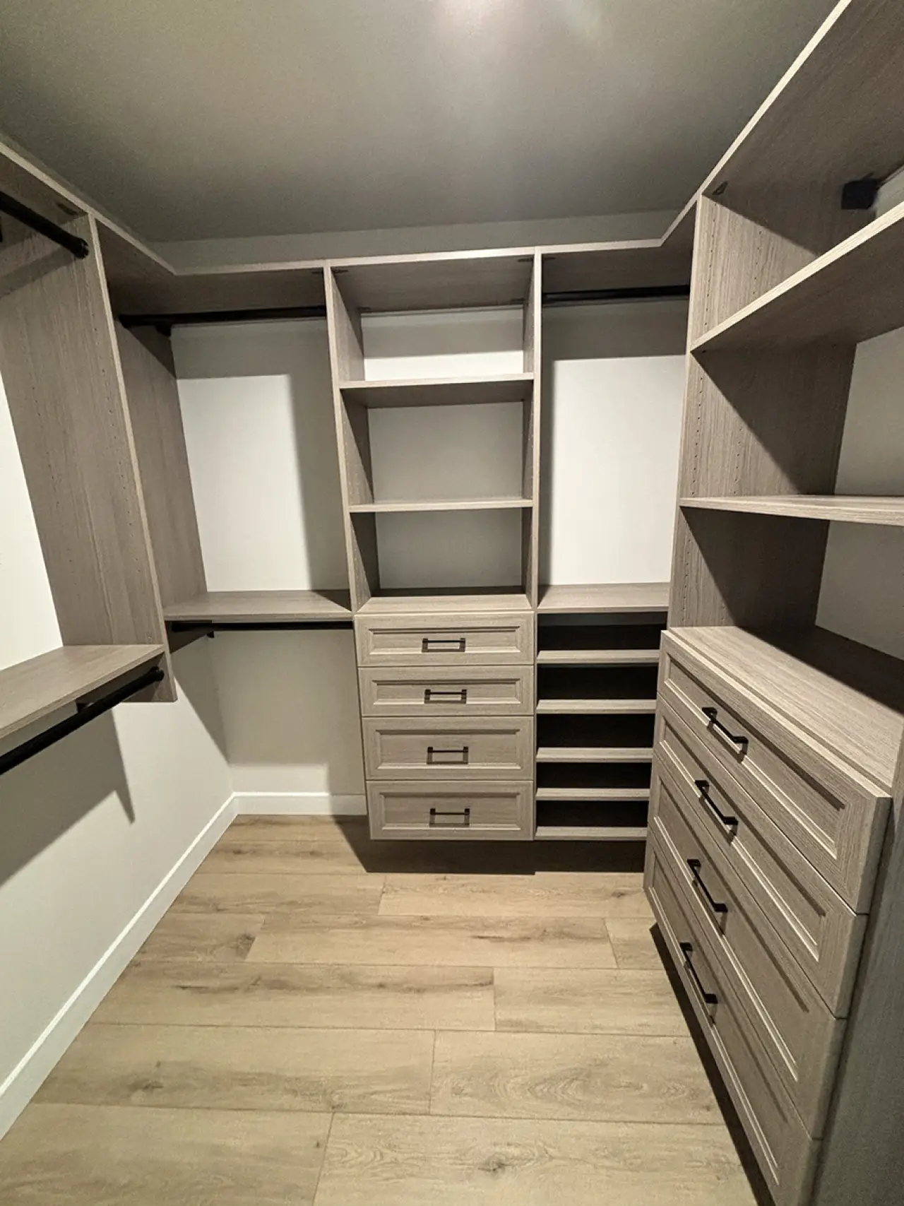 Modern walk-in closet with wood shelves, drawers, and hanging rods on light wood flooring.