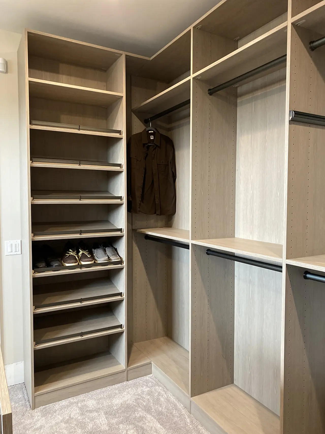 Empty walk-in closet with shelves, a few shoes, and a brown jacket hanging on a rod.