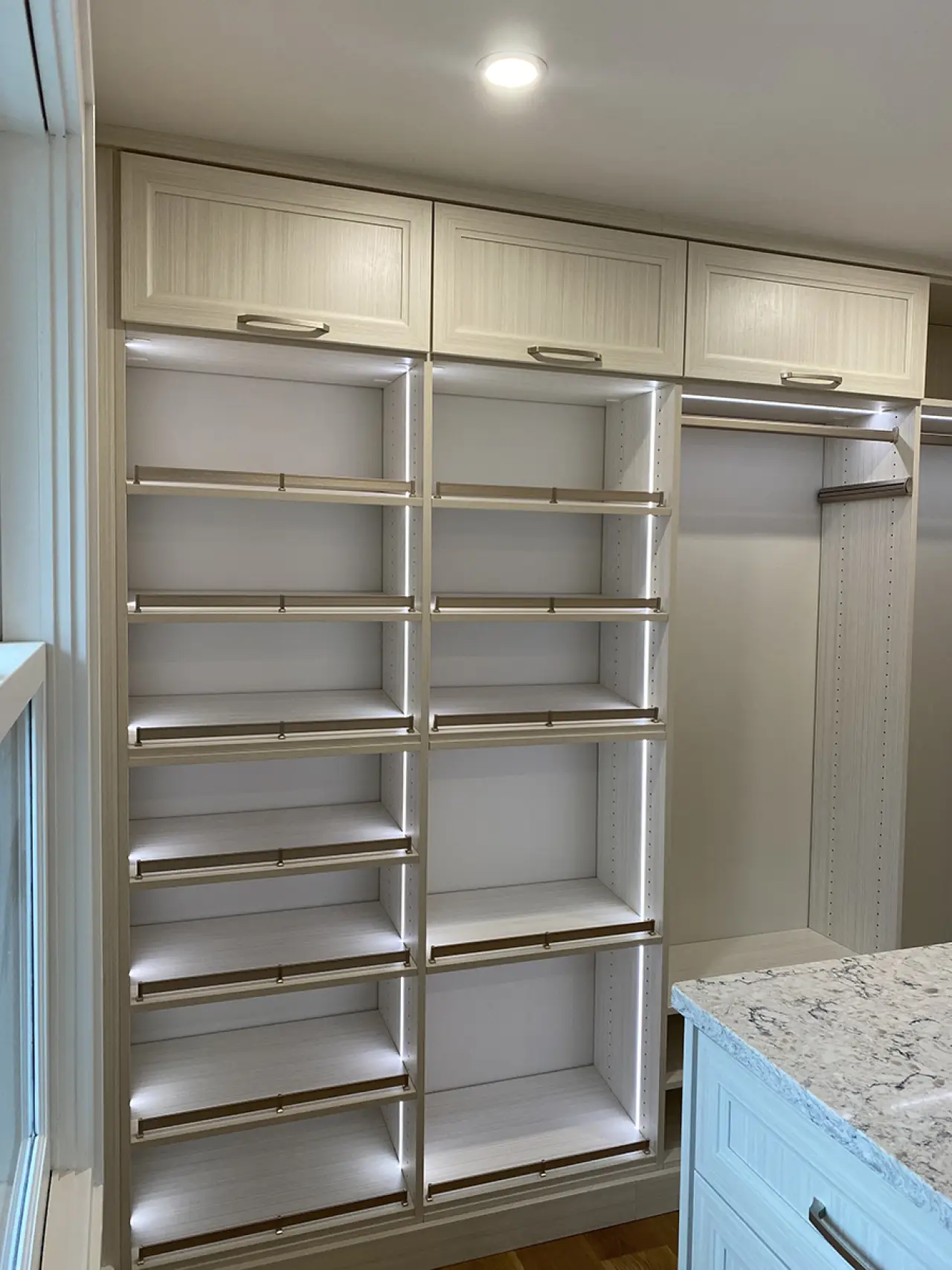 Built-in closet with empty shelves, hanging rods, upper cabinets, and LED lighting.
