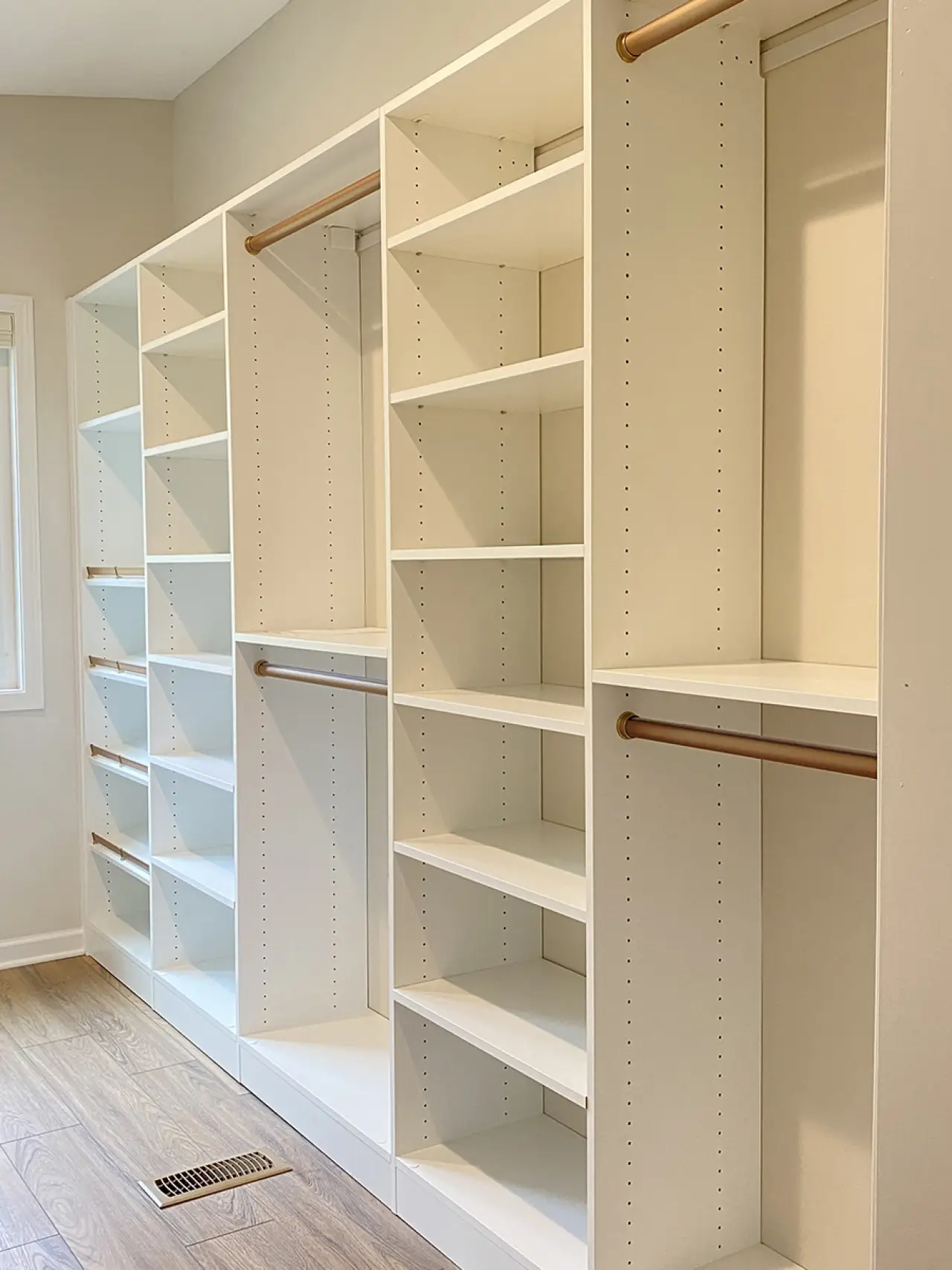White built-in closet shelves and hanging rods in an empty, well-lit room with wood flooring.