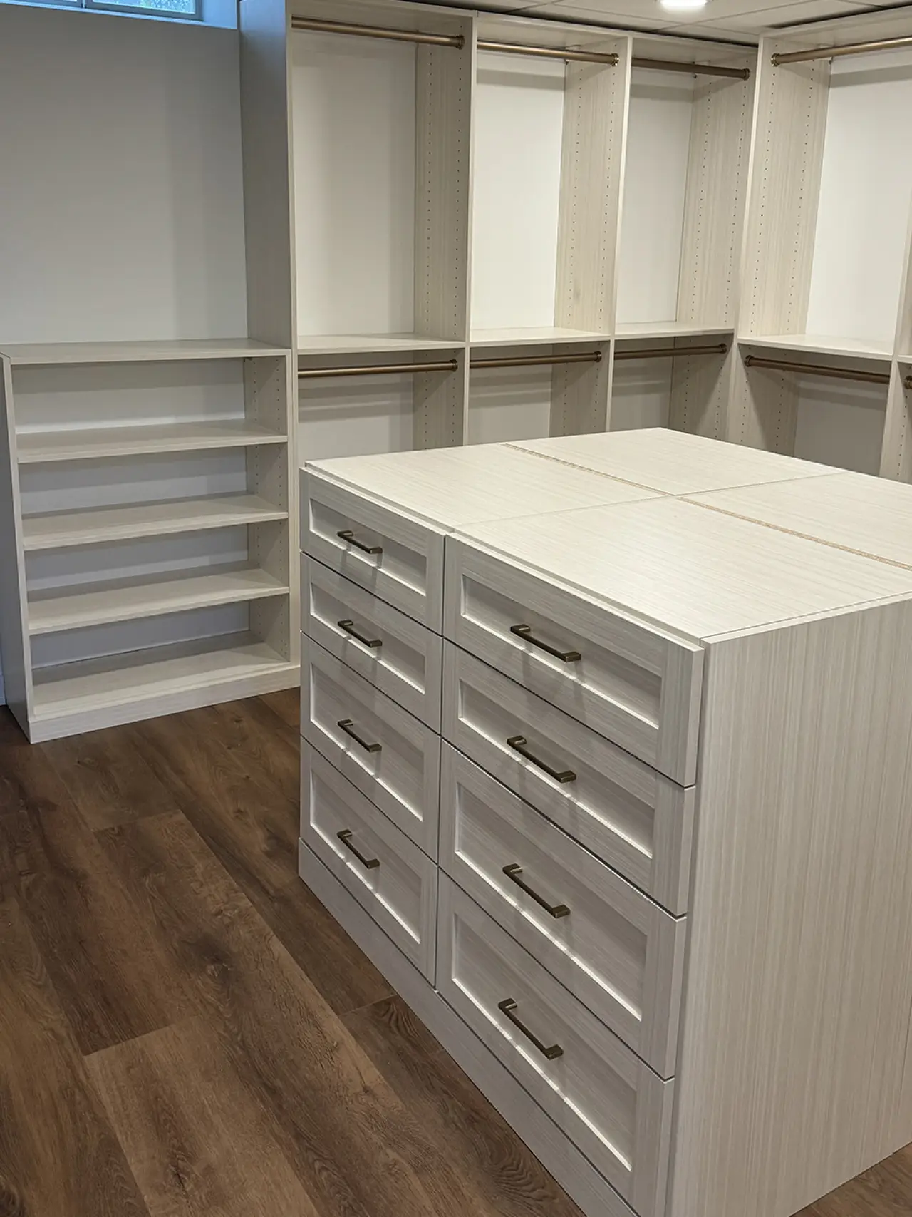 Walk-in closet with open shelves, empty hanging rods, and an island of drawers in the center.