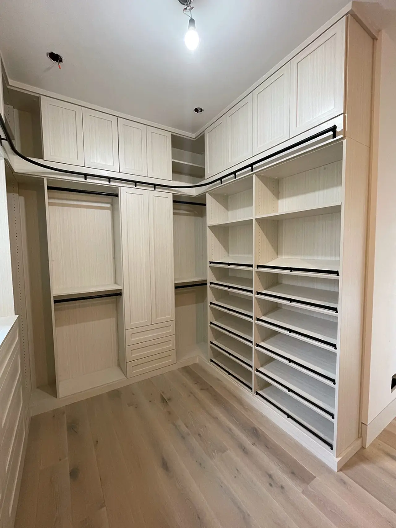 Spacious walk-in closet with light wood shelves, drawers, cabinets, and hanging rods.