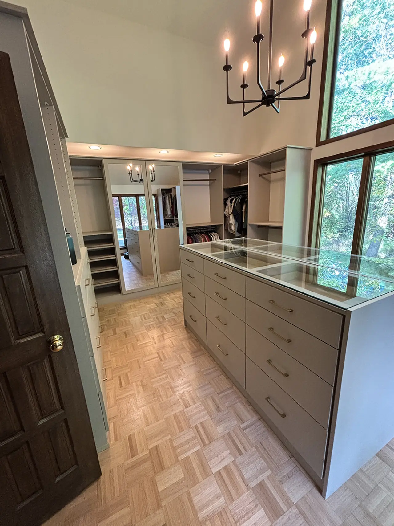 Spacious walk-in closet with large dresser, hanging clothes, mirrors, and tall windows.