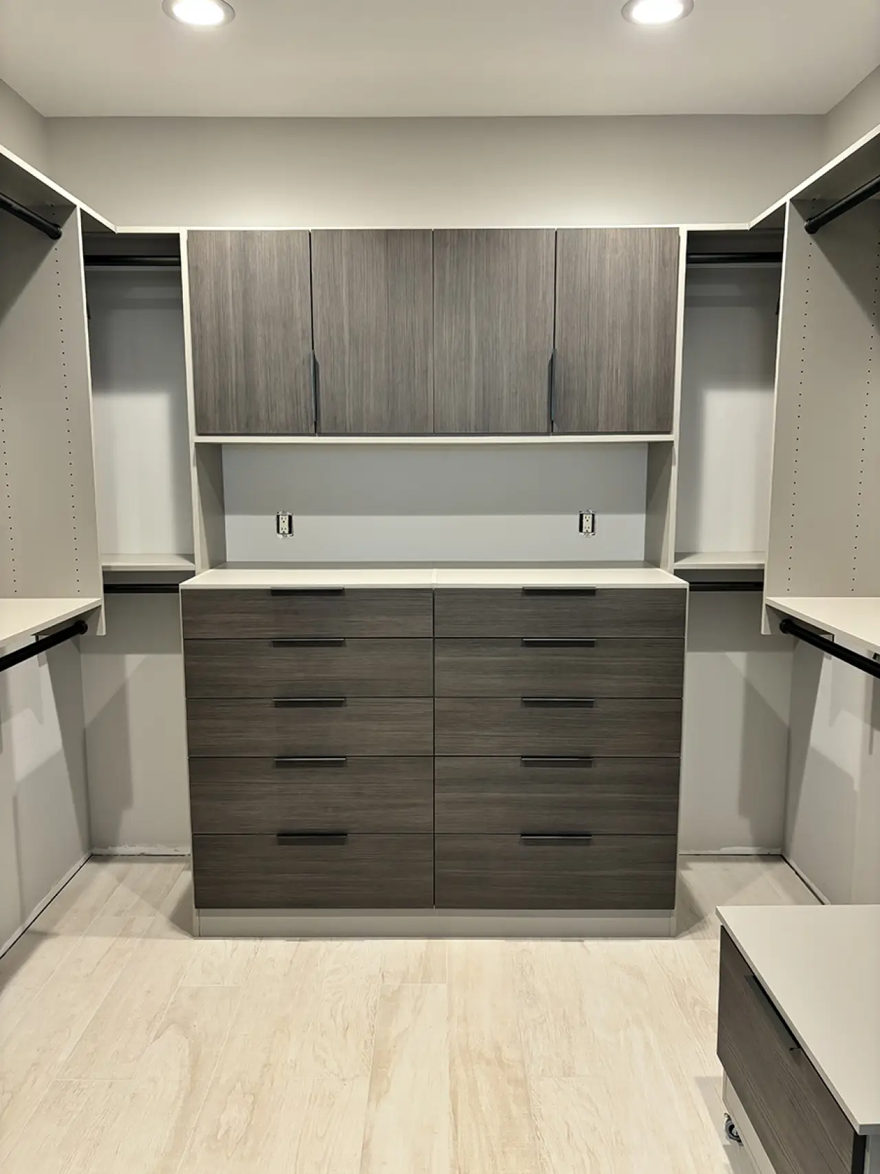 Modern walk-in closet with gray wood cabinets, drawers, shelves, and light wood flooring.