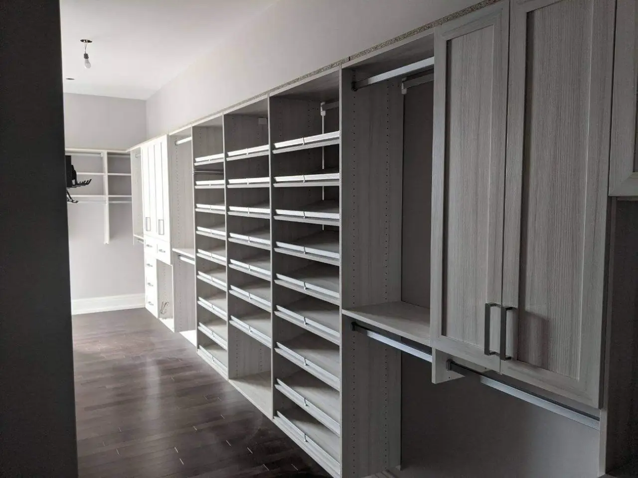 Spacious walk-in closet with empty shelves, cabinets, and hanging rods along both walls.
