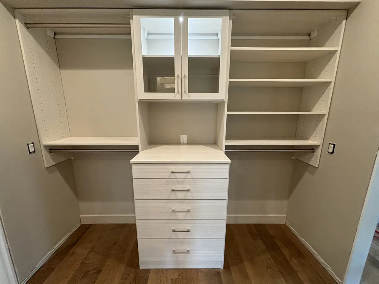 Custom closet with drawers, shelves, and hanging rods, in a white wood finish on hardwood floor.