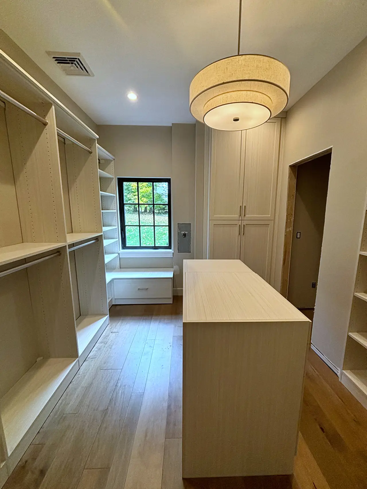 Walk-in closet with built-in shelves, center island, window seat, and modern light fixture.