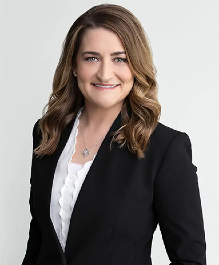 Woman with wavy brown hair in black blazer and white blouse, smiling at the camera.