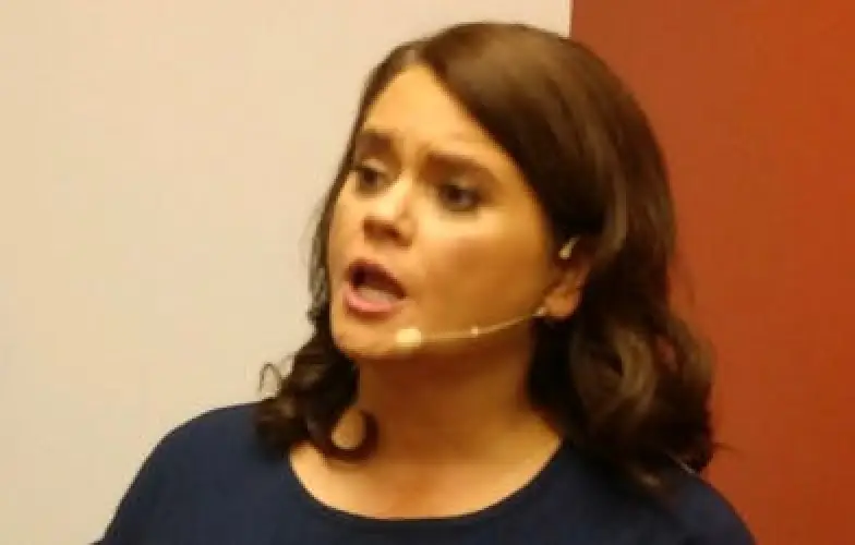 Woman with brown hair speaking into a headset microphone against a white and red background.