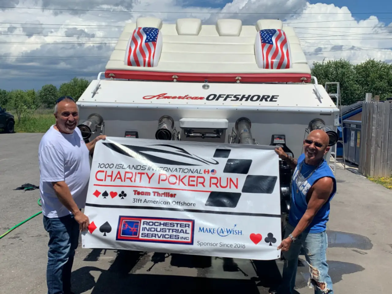 Two men hold a charity poker run banner behind a speedboat with American flag seat covers.