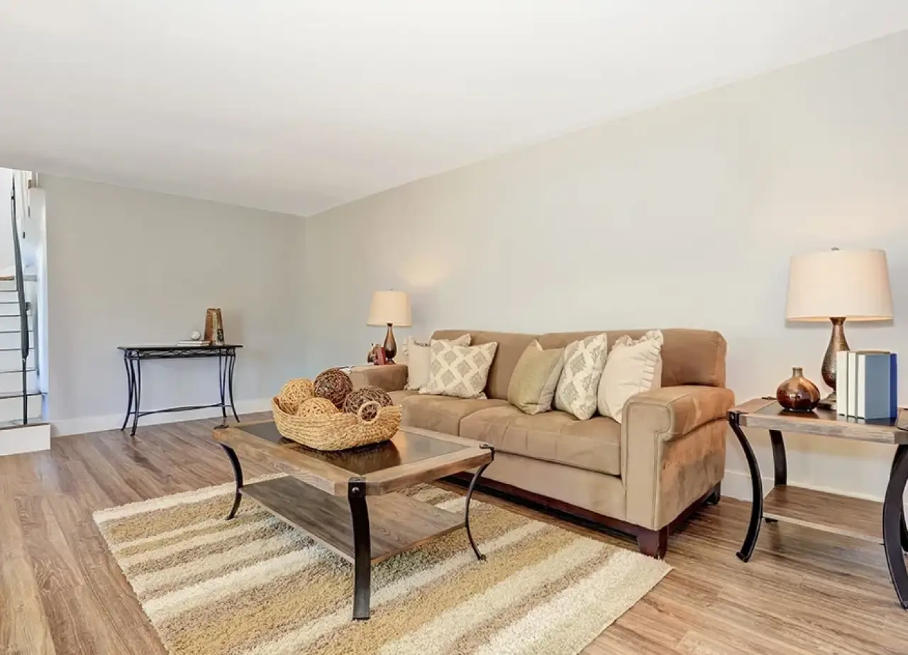 Modern living room with a brown sofa, coffee table, lamps, and striped rug on wooden floor.
