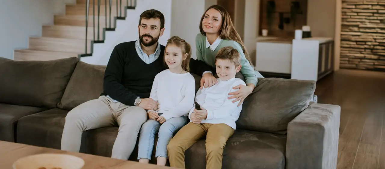 A family of four sits and smiles together on a couch in a modern living room.