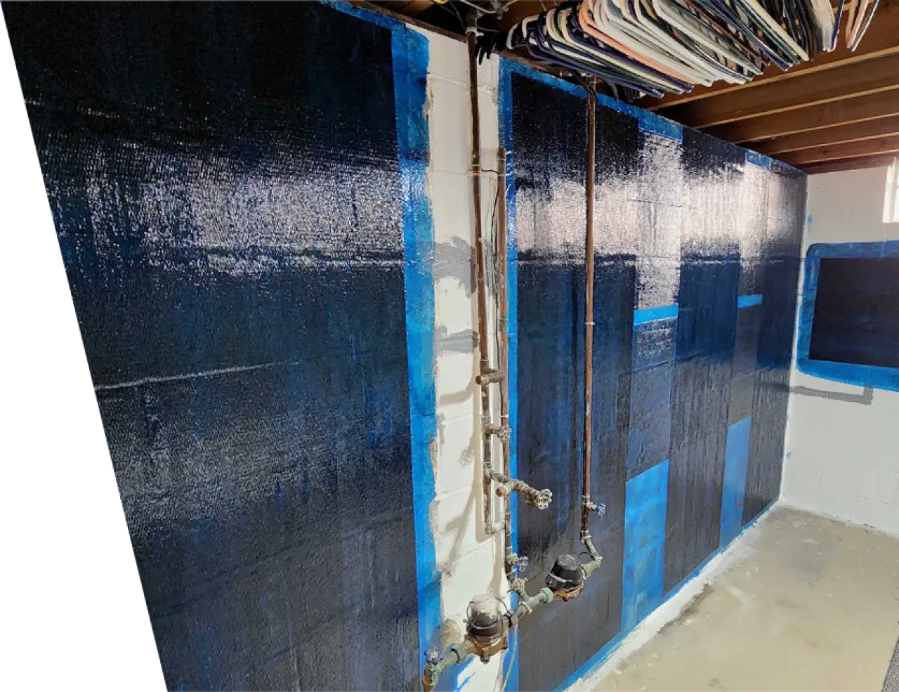Basement wall with blue-black panels, exposed pipes, and clothing hangers on the ceiling.
