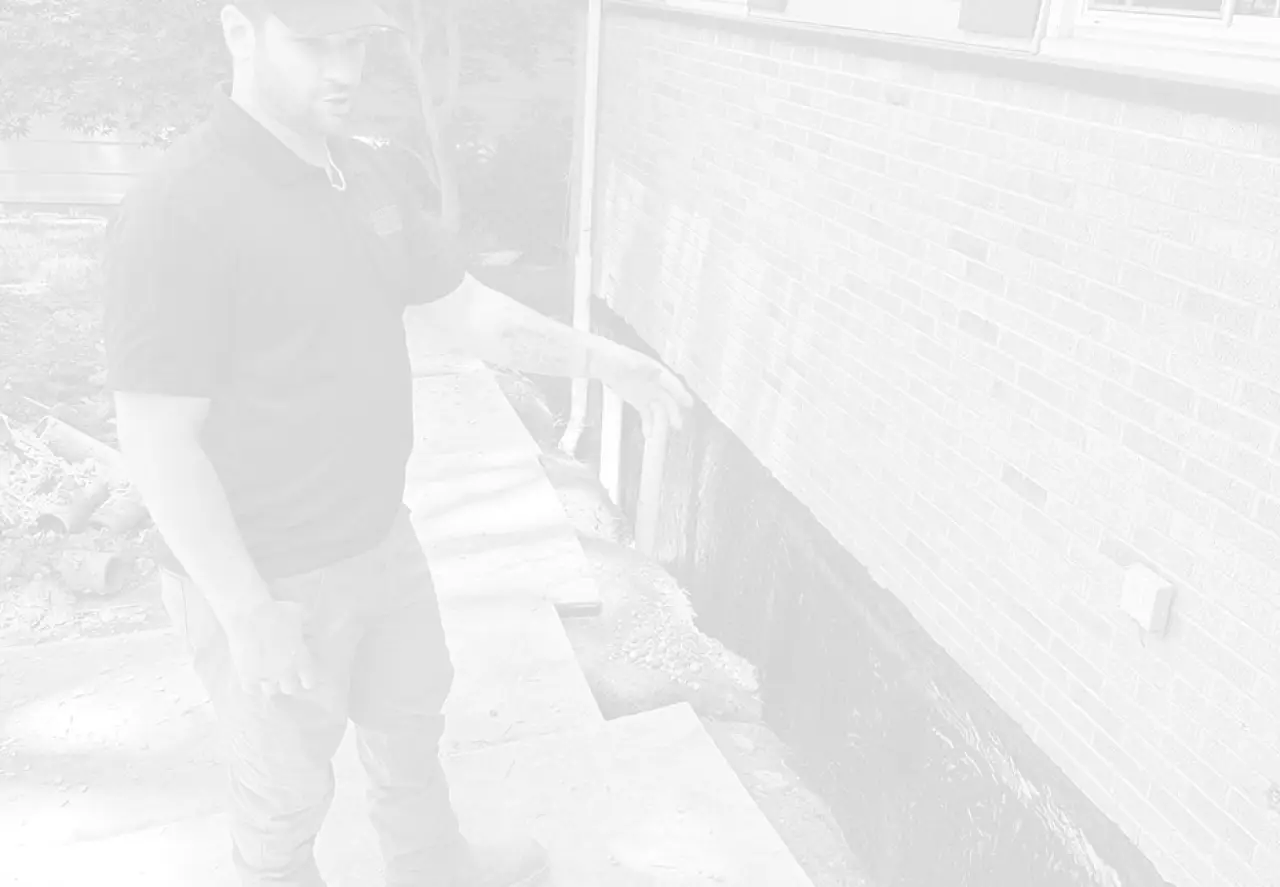 A man gestures toward the foundation of a brick building near a concrete walkway.