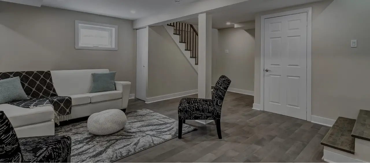 Modern finished basement with a sofa, chairs, rug, and stairs leading upstairs.
