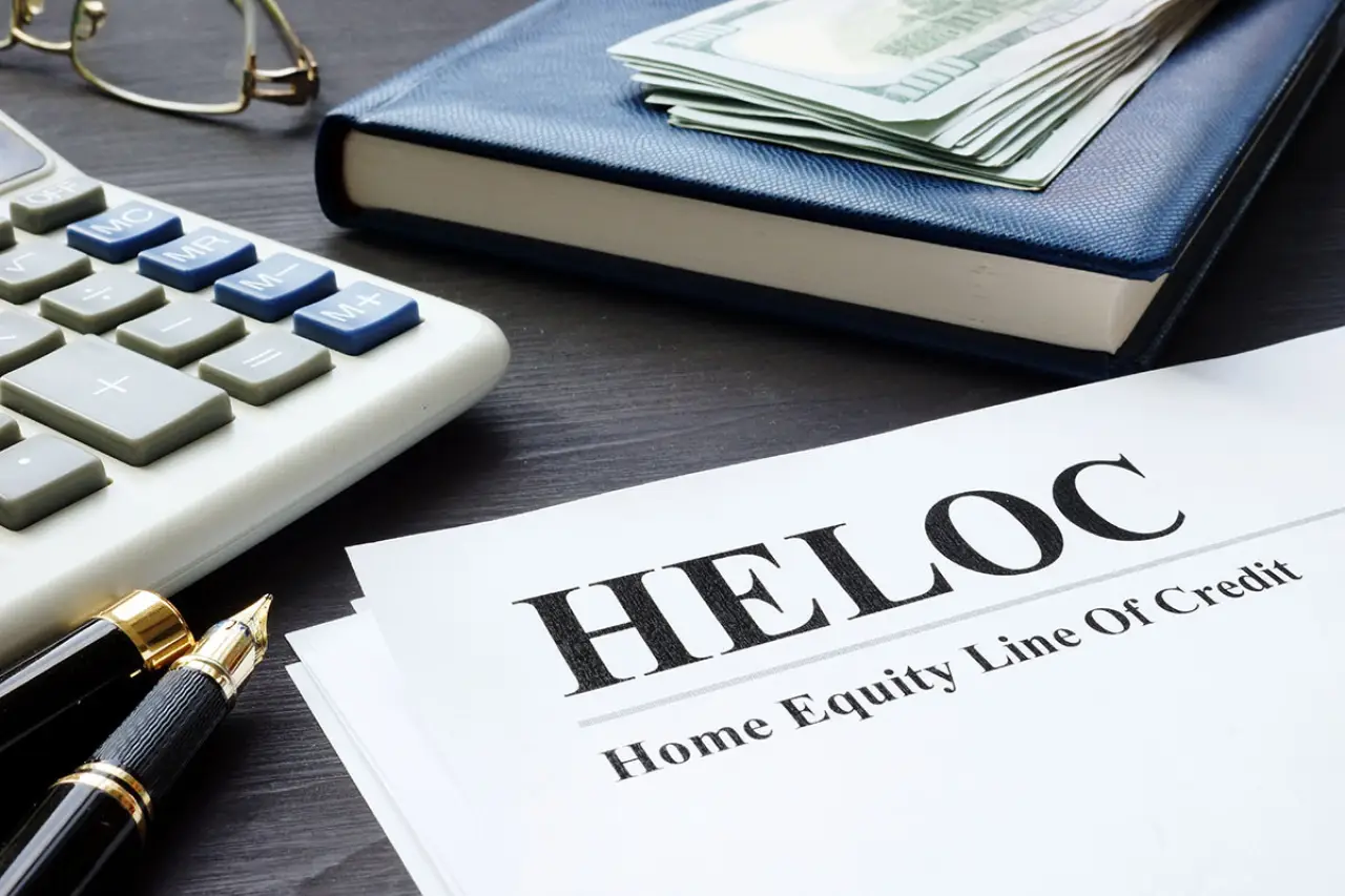 A HELOC document on a desk with a pen, calculator, notebook, and cash.