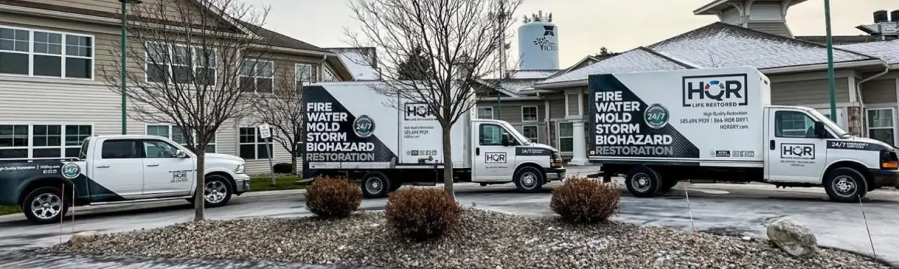 Three restoration service trucks parked outside buildings on a cloudy day.