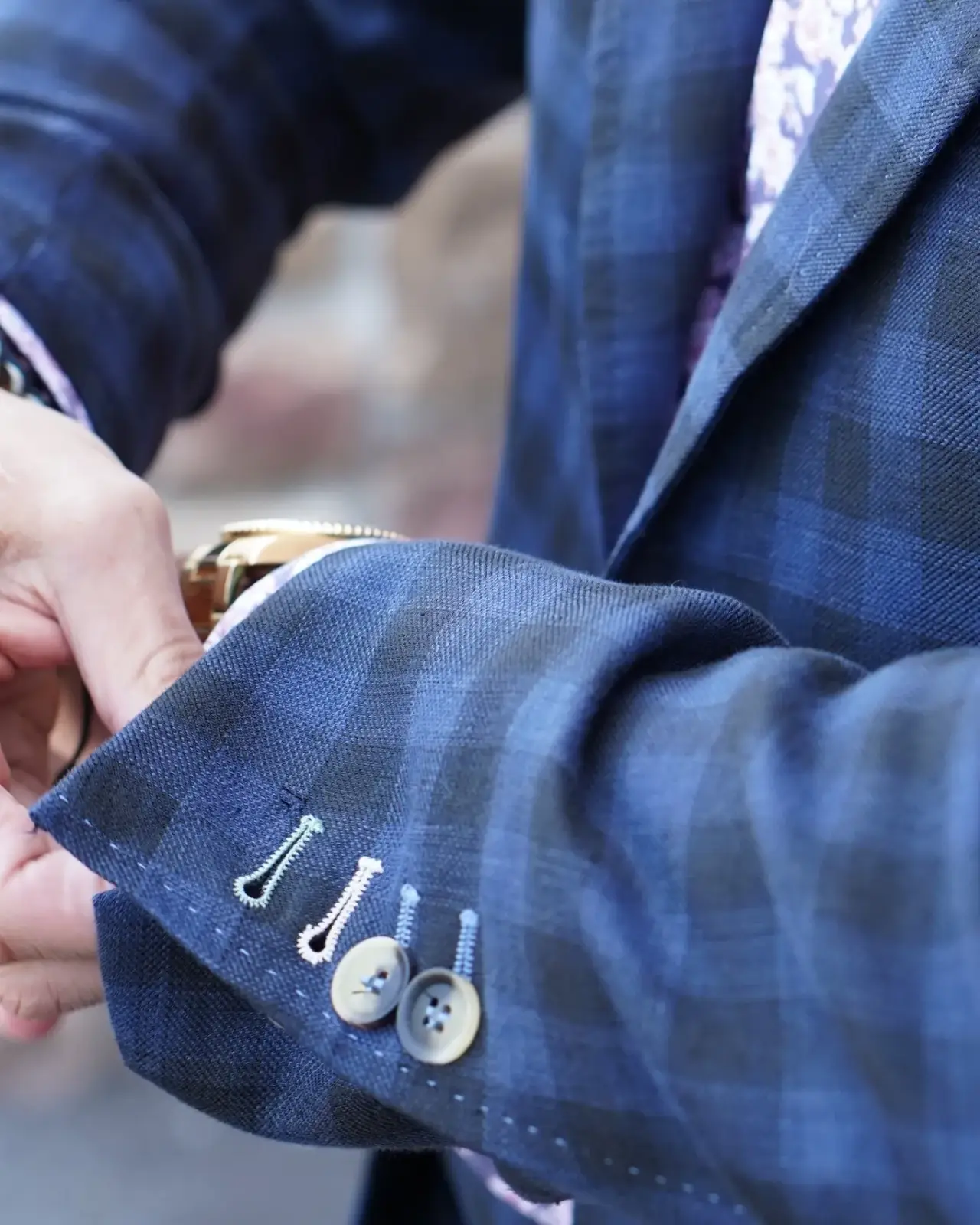 Close-up of a blue suit sleeve with buttons and stitching.