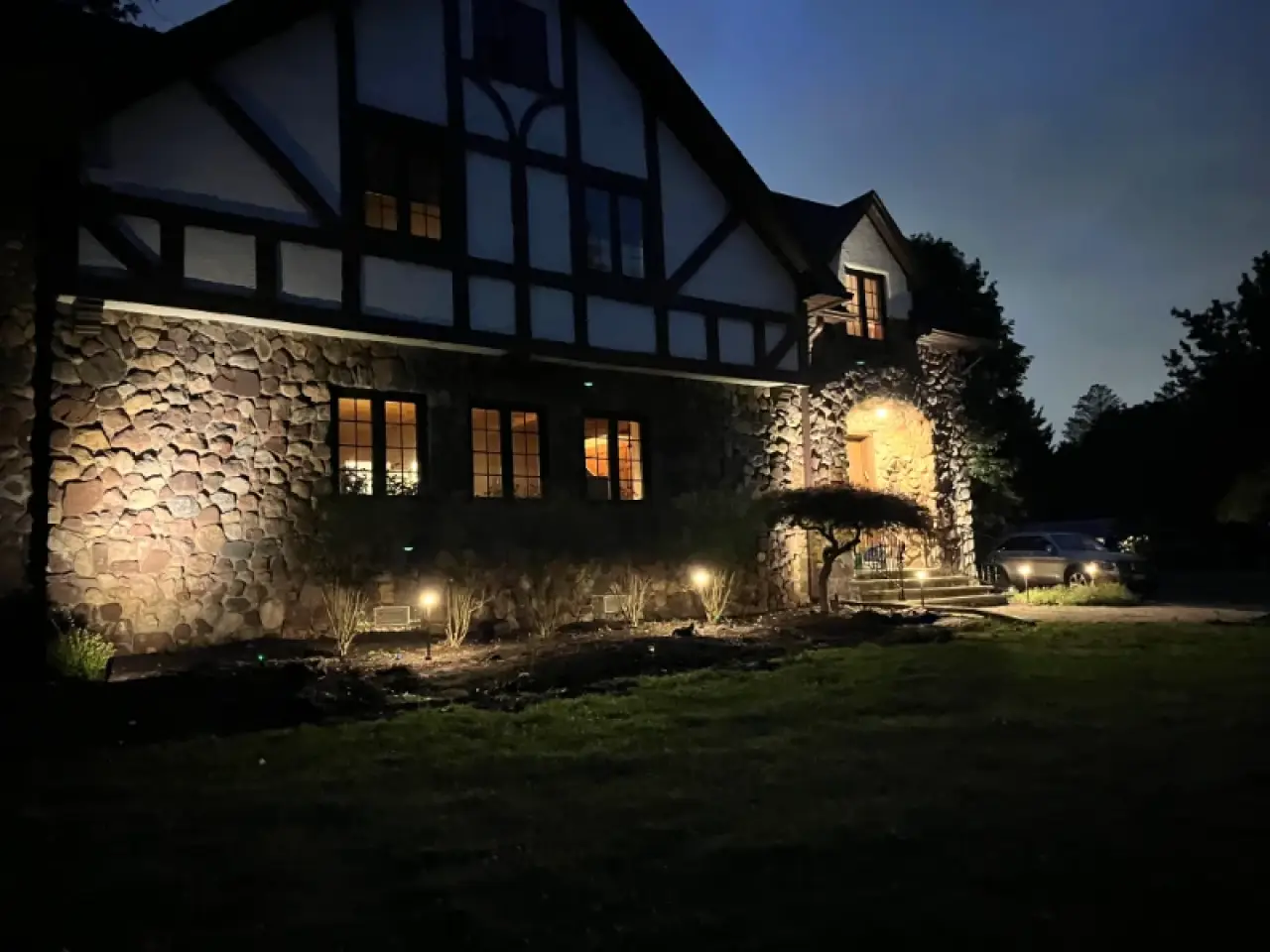 A square fire pit glows on a patio at night, with steps and garden lights in the background.