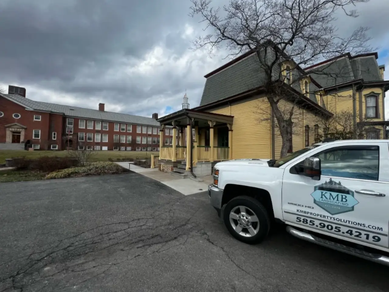 A white KMB truck parked beside a yellow house with a brick building in the background.